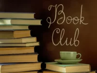 Book Club icon. A stack of books on the left with one book on the lower right with a green coffee cup sitting on it. The background is a dark golden brown. The books are muted but rich shades of brown and green. Above the coffee cup are the words, Book Club written in a flowy script.