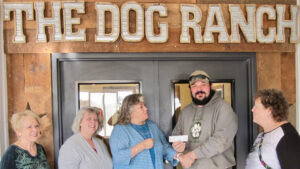 Five people, four women and one man stand in front of grey double doors. There is a sign above that says, The Dog Ranch